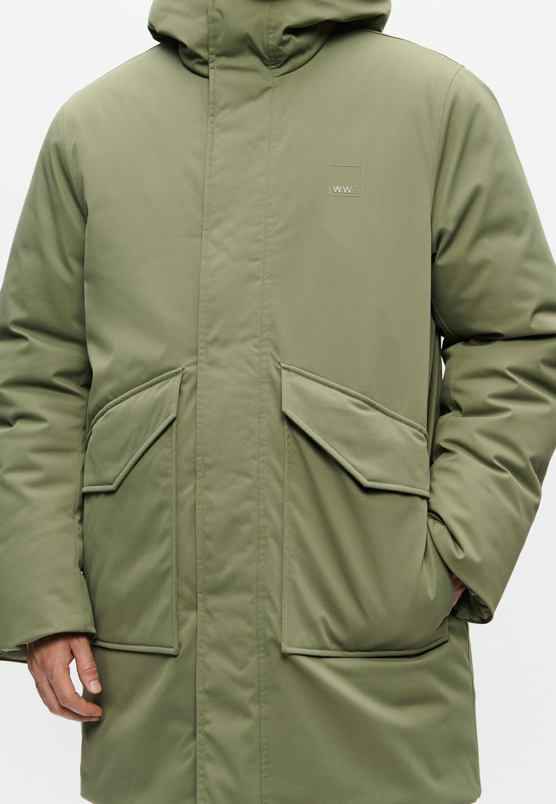 Chaqueta acolchada de color verde oliva con capucha, que cuenta con grandes bolsillos frontales, un cierre frontal sellado y un discreto logotipo en el pecho.