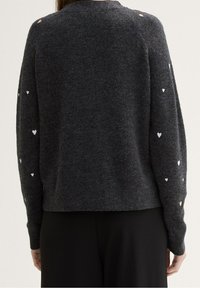 Šedý pletený svetr s dlouhými rukávy a vzorem srdcí v bílé a zlaté barvě. Měkká textura, uvolněný střih a kulatý výstřih.