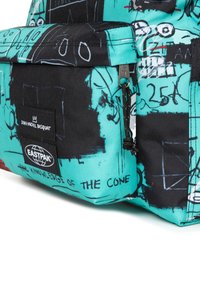 Reppu, jossa on turkoosi ja musta graafinen muotoilu, johon on piirrettyjä kuvastoja ja tekstiä. Valmistettu kestävästä kankaasta, sisältää Eastpak- ja Jean-Michel Basquiat -logot.