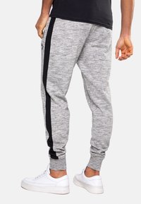 Gray fleece joggers feature a black side stripe. The elastic waistband and cuffs provide a snug fit. Styled with white sneakers.