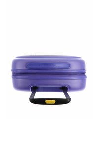 Valise rigide de couleur violette avec deux poignées extensibles. Dotée d'une fermeture éclair et d'une surface texturée, agrémentée d'une poignée noire et jaune.
