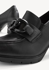 Mocassins pour femmes en cuir noir avec talons carrés bas et grand détail de chaîne reliée sur le dessus avant.
