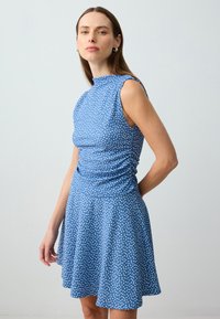 Blaues ärmelloses Kleid mit weißen Punkten, tailliertem Oberteil und weit schwingendem Rock. Weicher Stoff mit leichter Raffung an der Taille.