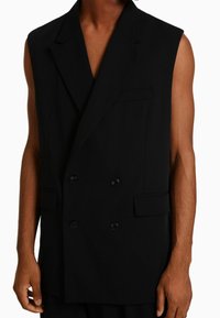Svart dubbelknäppt väst utan ärmar, tillverkad av ett glansigt tyg, med två framfickor och svarta knappar.
