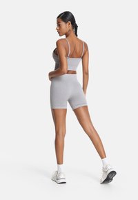 Sivina športna kombinacija, ki vključuje prilegajoč se krajši zgornji del in ustrezne kratke hlače z visokim pasom. Tkanina je raztegljiva z gladko teksturo. Obute so bele superge.