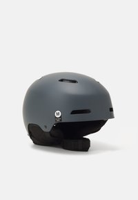 Casco grigio opaco con fessure di ventilazione, cinturino regolabile e etichetta di taglia (M, 55-59 cm). Superficie liscia e design arrotondato.