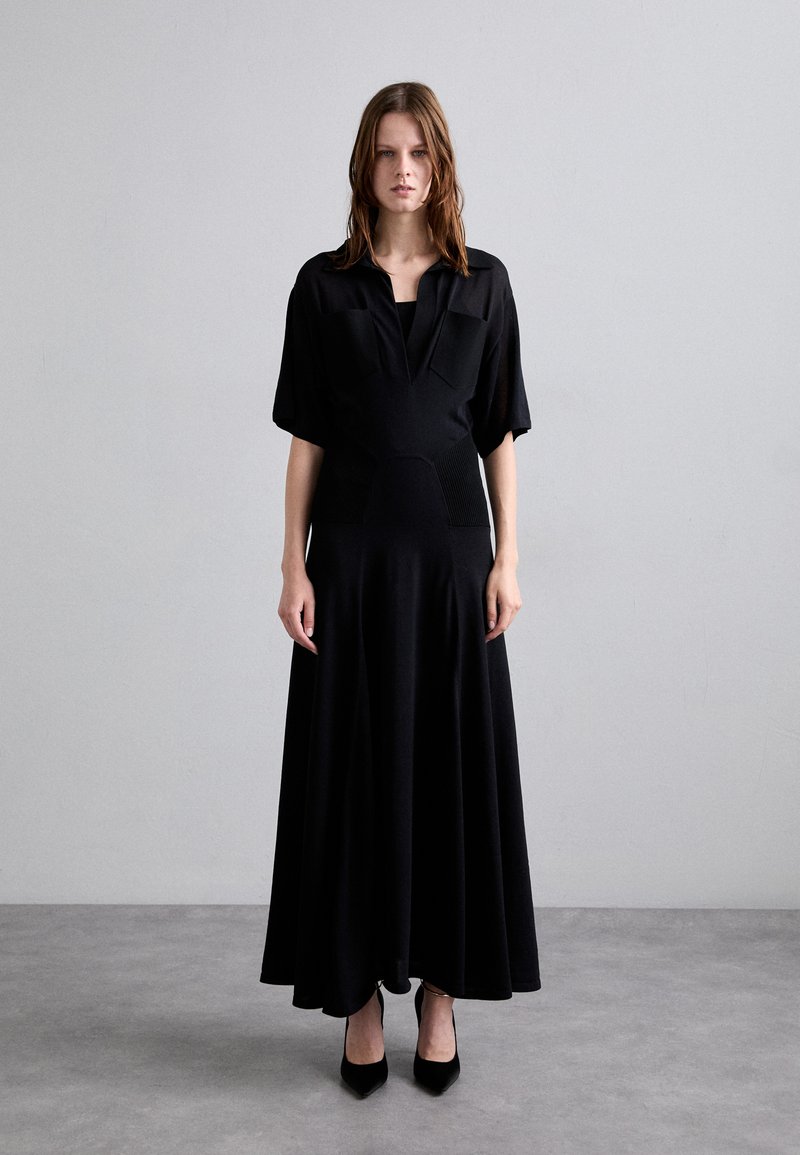 Vestito nero a maniche lunghe realizzato in tessuto morbido, con colletto e corpino aderente che si allarga in una gonna ampia.