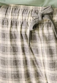 Sive i bijele karirane hlače za opuštanje s mekim, teksturiranim materijalom. Imaju elastičnu waistband i trakicu od istog materijala.