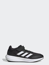 Zapatilla deportiva negra con parte superior de malla texturizada y un diseño de tres franjas blancas en contraste. Presenta una correa de Velcro y una suela blanca gruesa.
