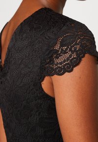 Svart spetsklänning med blommönster, korta scallopärmar och öppen ryggdesign med dragkedjestängning.