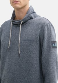 Grijze sweatshirt met een col, voorzien van een gestructureerde afwerking, elastische koorden met kleuraccenten en een merkembleem op de mouw.
