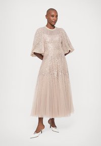 Jasnoróżowa sukienka maxi z krótkimi bufkami, ozdobiona cekinami, z warstwową spódnicą z tiulu, w połączeniu z białymi szpilkami w szpic.