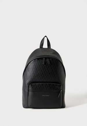 Sac à dos en cuir noir avec motif embossé, poche zippée à l'avant et poignée supérieure, sur un fond gris clair uni.