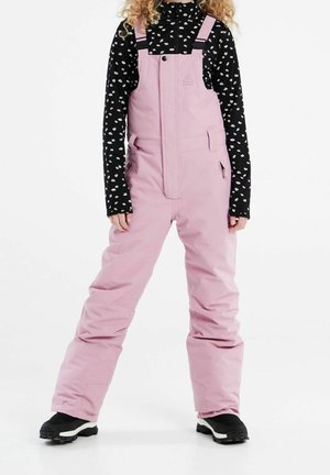 Enfant portant une salopette de neige isolante rose et un haut à manches longues noir à fleurs, debout jambes écartées sur un fond blanc.