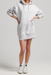 Graues, übergroßes Hoodie-Kleid mit einer vorderen Kängurutasche, langen Ärmeln und einer Kordelzugkapuze, kombiniert mit weißen High-Top-Sneakern.