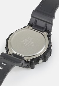 Bracelet en résine noire avec un fond de montre en acier inoxydable. Présente une forme ronde, des accents texturés et du texte gravé au dos. Résistant à l'eau.