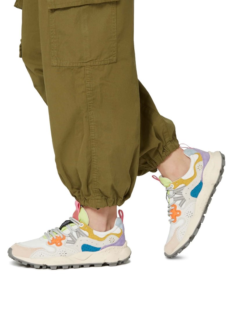 Sneaker multicolore con parte superiore bianca e dettagli pastello, suola chunky e hardware unico, abbinata a pantaloni cargo color oliva.