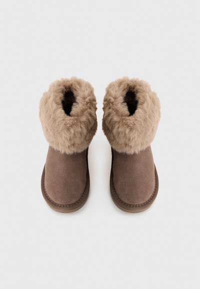 Botas cortas marrones de ante con un suave puño de piel de pelo beige en la parte superior, con una punta redondeada lisa y una suela de goma plana.