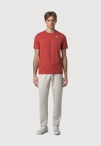 T-shirt rossa in cotone con collo rotondo e maniche corte, abbinata a pantaloni della tuta beige chiaro e scarpe da ginnastica bianche.