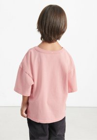 Lyserød oversized T-shirt med rund halsudskæring og korte ærmer, lavet af blødt bomuldsstof. Båret med mørke strukturerede fløjl-bukser.