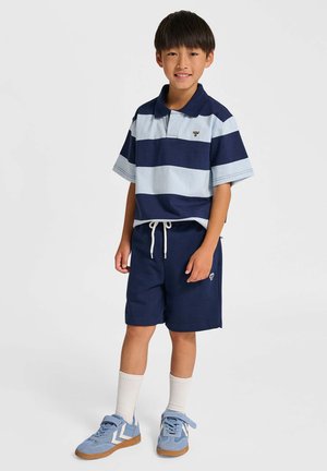 Kurzärmliges Poloshirt mit marineblauen und hellblauen Streifen, kombiniert mit marineblauen Shorts. Blaue Sneaker, weiße Socken und Logodetails auf beiden.