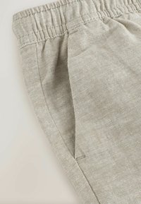 Pantalones de tela de lino beige con cintura elástica y bolsillo lateral con costura visible.