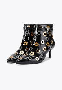 Czarne lakierowane botki za kostkę z wydłużonymi noskami, ozdobione metalowymi oczkami w złotym i srebrnym kolorze. Zawierają wąski obcas oraz szczegóły z ankle strap.