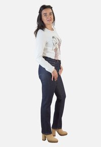 Blusa blanca de manga larga con un estampado gráfico, combinada con jeans rectos de color azul oscuro y tacones de plataforma beige.
