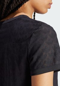 Fekete textúrájú póló, kis geometriai formák mintázatával, szilárd fekete díszítéssel az ujjakon és a nyakrészen.