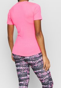 Camiseta ajustada de manga corta en rosa brillante, hecha de tela suave. Combinada con leggings negros estampados con detalles en rosa y blanco.
