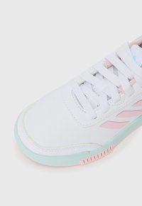 Weißer Sportschuh mit pinken und mintfarbenen Akzenten. Verfügt über ein glattes Synthetik-Obermaterial, eine Schnürung und eine strukturierte Sohle mit Rillenmuster.