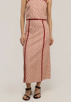 Mujer con un vestido blanco sin mangas con un pequeño estampado floral rojo y rayas verticales rojas, combinado con sandalias negras con tiras en el tobillo.