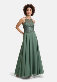 Długa zielona sukienka wieczorowa z koronkowym gorsetem z połyskiem, dekoltem halter, zwiewną spódnicą i falbaniastym dołem.