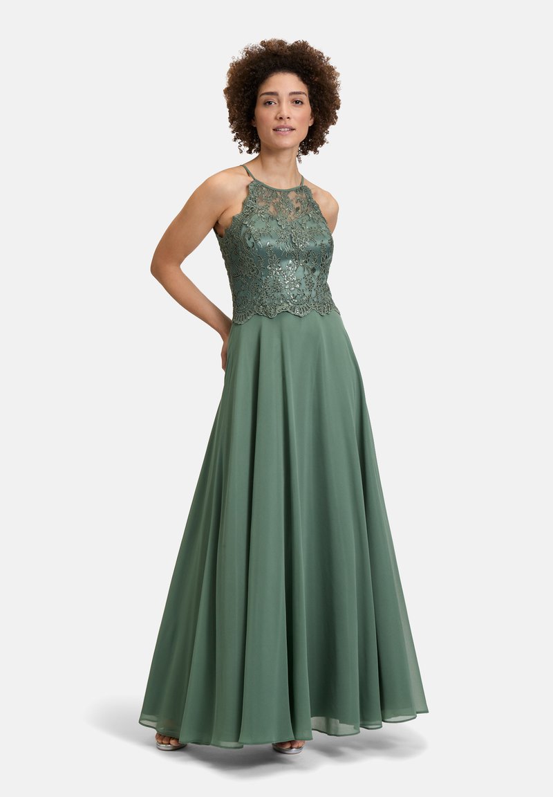 Długa zielona sukienka wieczorowa z koronkowym gorsetem z połyskiem, dekoltem halter, zwiewną spódnicą i falbaniastym dołem.