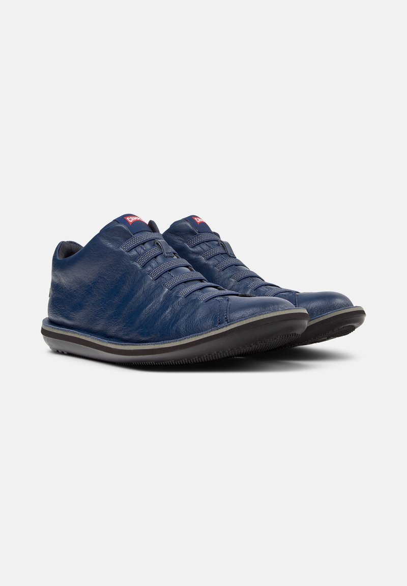Donkerblauwe sneakers met elastische veters en een gestructureerde leren afwerking, zij aan zij gepositioneerd op een effen achtergrond.