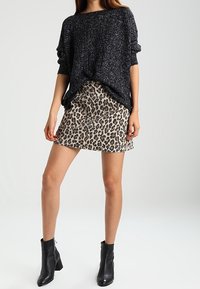 Maglione a maglia nero maculato, vestibilità ampia con maniche arrotolate, abbinato a una mini gonna leopardata color beige. Stivaletti neri con tacco a blocco.