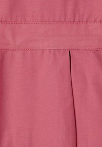 Tissu couleur rose avec une texture lisse; présente des plis horizontaux et verticaux, avec des accents cousus le long des coutures.