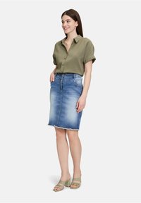 Licht olijfgroene kolber voor met opgerolde mouwen, gecombineerd met een middellange vervaagde blauwe denimrok met een ruwe zoom en lichte slijtage.