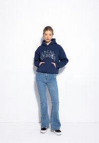 Granatowy hoodie z napisem "LOKALNI BOHATEROWIE" w kolorze srebrnym, z przednią kieszenią i szerokimi rękawami, w połączeniu z jasnoniebieskimi dzwonami.