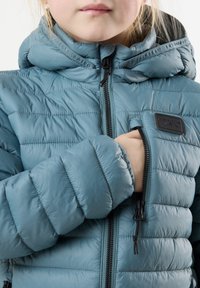 Ljusblå vadderad jacka med hög krage, blixtlås framtill och en liten bröstficka. Har kviltad textur och justerbara dragsnören på huvan.