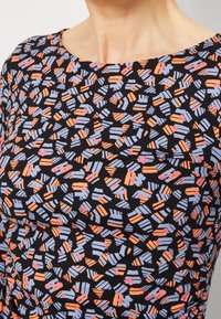 Svart tyg topp med ett abstrakt mönster av orange och ljusblå former, med en rundad halsringning och korta ärmar.