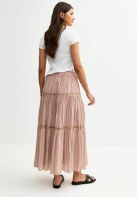 Lichtroze, gelaagde maxi-rok van zacht stof, met kantdetails, gedragen met een aansluitend wit topje en zwarte sandalen.
