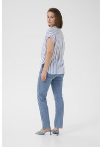 Haut à manches courtes rayé bleu et blanc, assorti à un jean bleu clair et à des talons ouverts assortis, sur fond blanc uni.