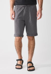 Grå shorts med snor i livet, rullet oppkant og myk tekstur, sammen med svarte sandaler med justerbare stropper.