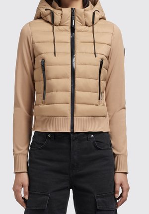 Beige quiltet hættejakke med sort lynlås og lommer, båret med sorte cargobukser.