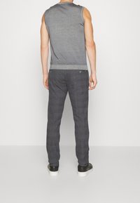 Šedý tílko bez rukávů s žebrovaným lemem, v kombinaci s tmavými károvanými kalhotami. Významné detaily zahrnují dvě zadní kapsy a hladký povrch.