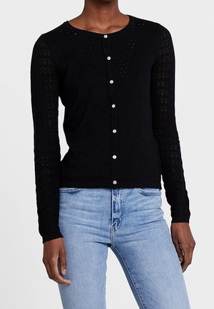 Czarny kardigan z okrągłym dekoltem, długimi rękawami o koronkowej fakturze oraz zapięciem na perłowe guziki. Nosi się go na niebieskie dżinsy.