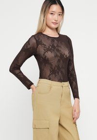Body in tessuto marrone a maniche lunghe con motivo floreale trasparente e testurizzato abbinato a pantaloni cargo beige con tasche laterali e dettagli con bottoni.