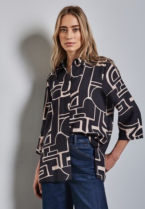 Schwarz-beige geometrisch gemustertes Hemd mit Knopfleiste, Dreiviertelärmeln und lockerer Passform, kombiniert mit blauen Jeans.