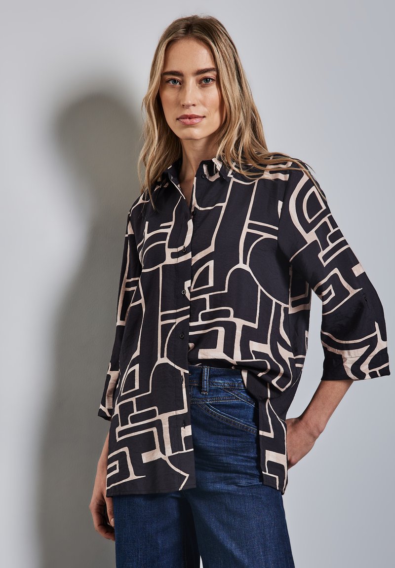 Camicia con motivo geometrico nero e beige, con bottoni davanti, maniche a tre quarti e vestibilità ampia, abbinata a jeans blu.